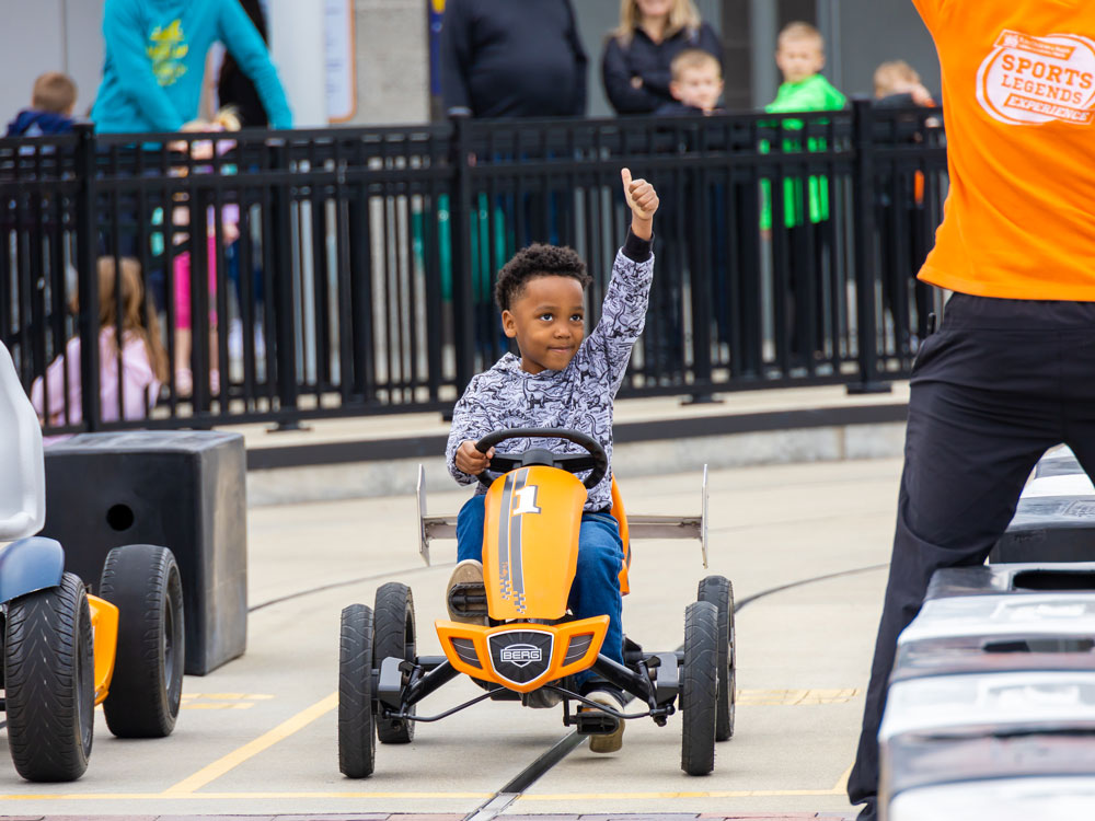 Child holding thumb up and ready to race in a pedal car.